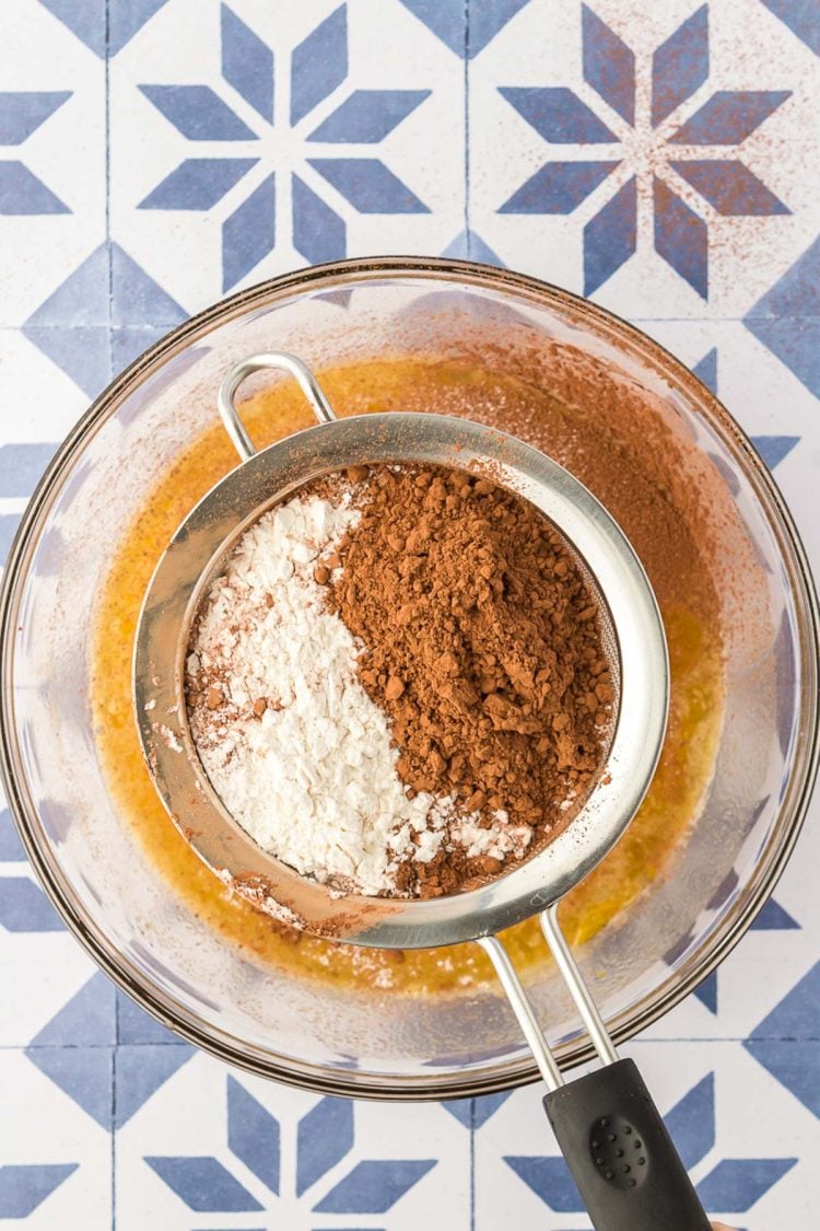 Flour and cocoa powder being sifted into a glass bowl to make brownies.