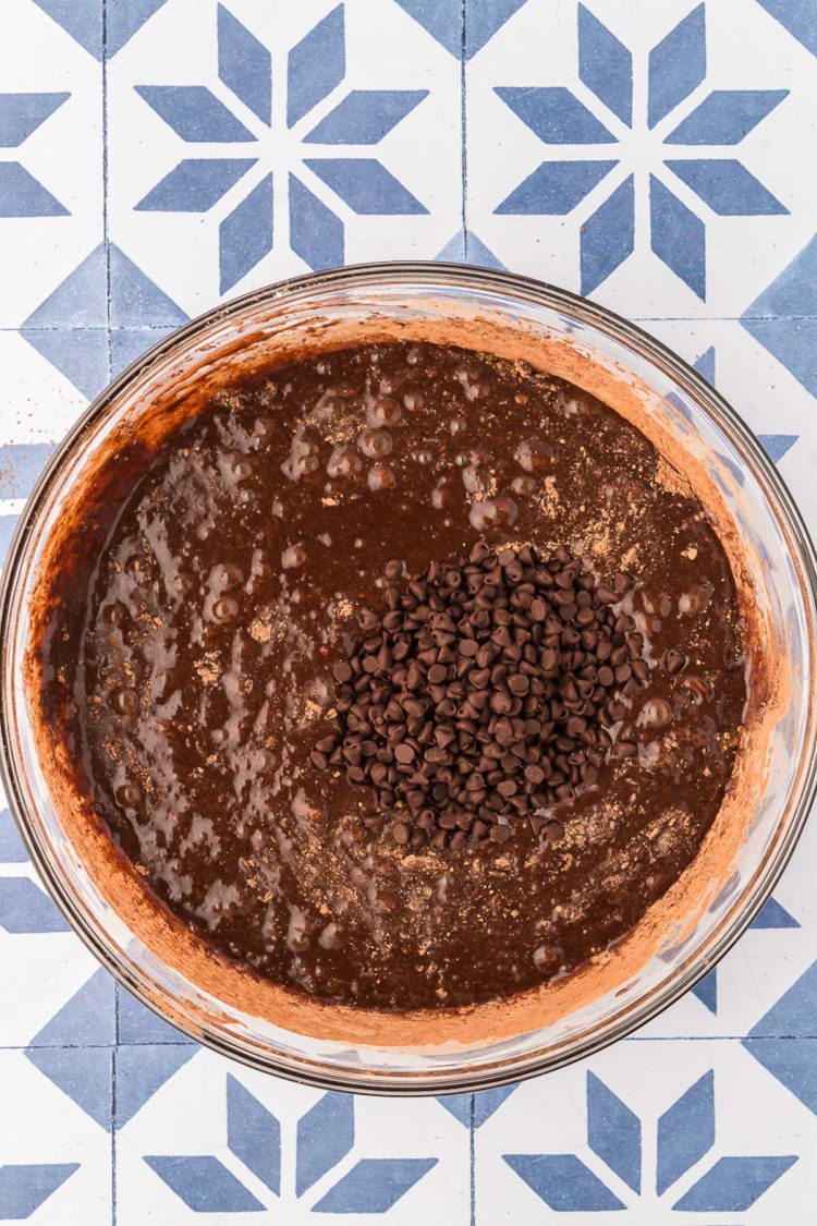 Chocolate chips being added to a glass bowl filled with brownie batter.