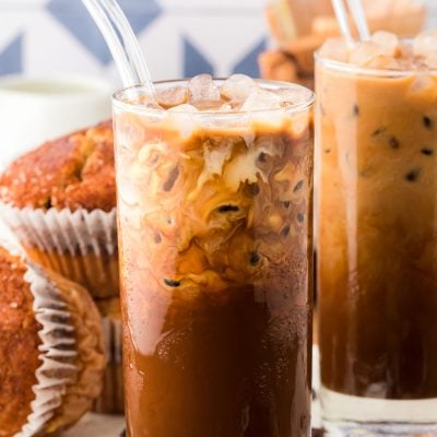 A glass of Thai Iced Coffee on a white serving board with more coffee and muffins in the background.