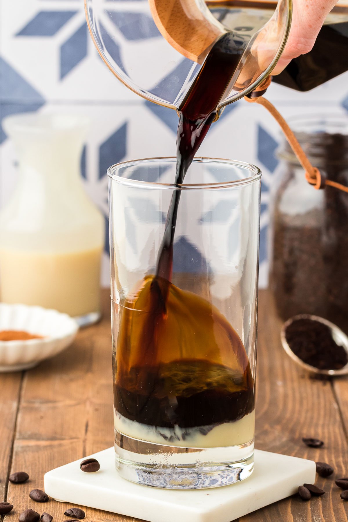 Thai coffee being poured into a tall glass with sweetened condensed milk.