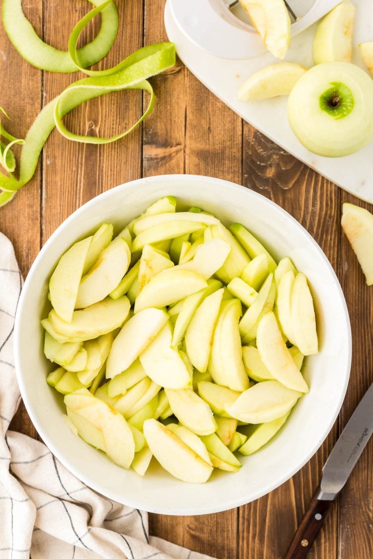 Peeled granny smith apples in a white bowl.