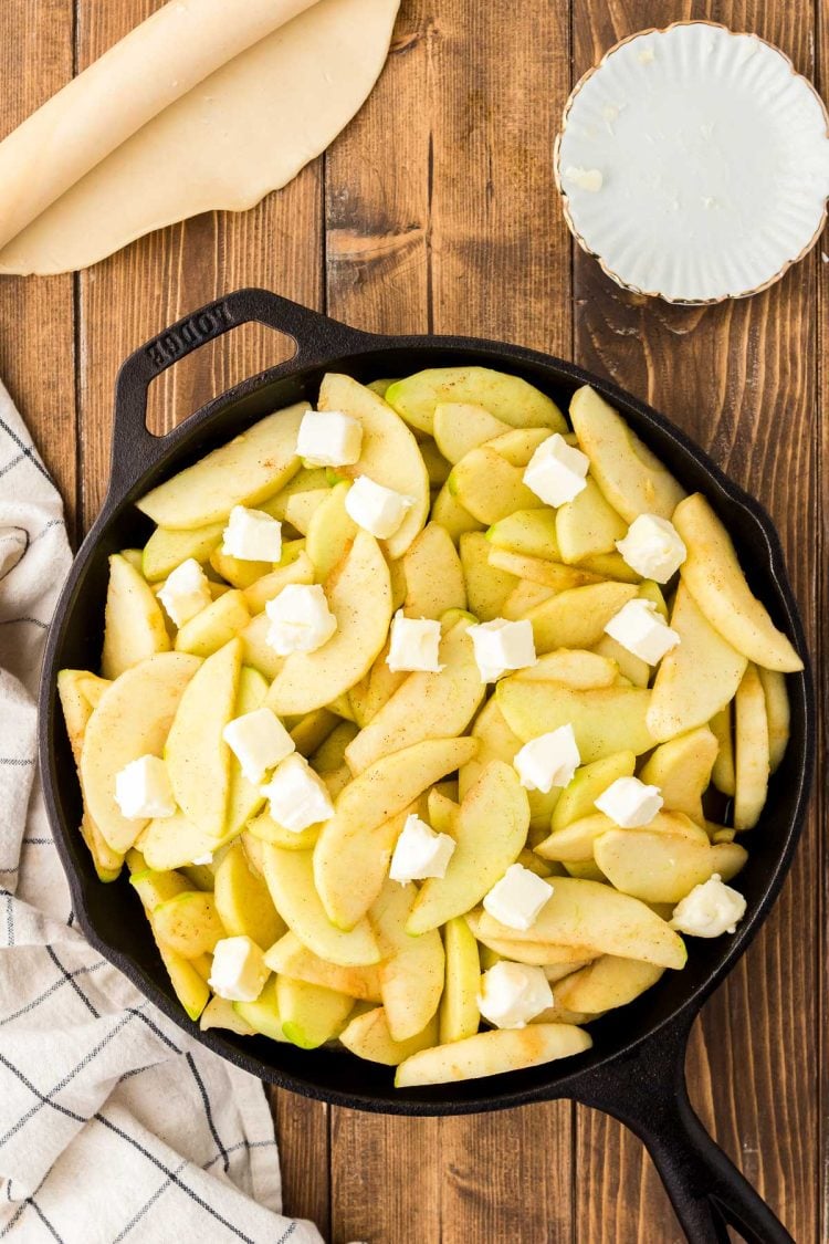 Cast iron skillet on a table with sliced apples and butter in it.