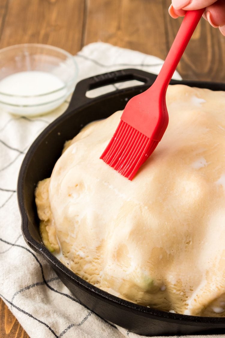 Milk being brushed over the top of pie crust.