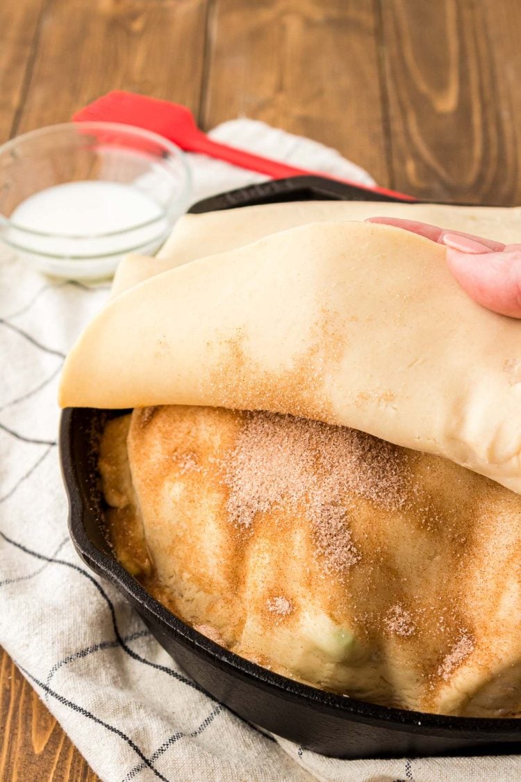 Pie crust being rolled over the top of another pie crust.