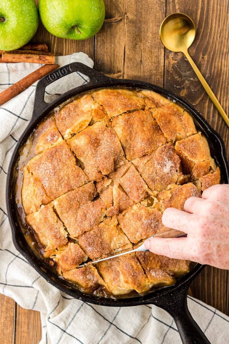 A woman's hand using a knife to cut the top of apple pandowdy.