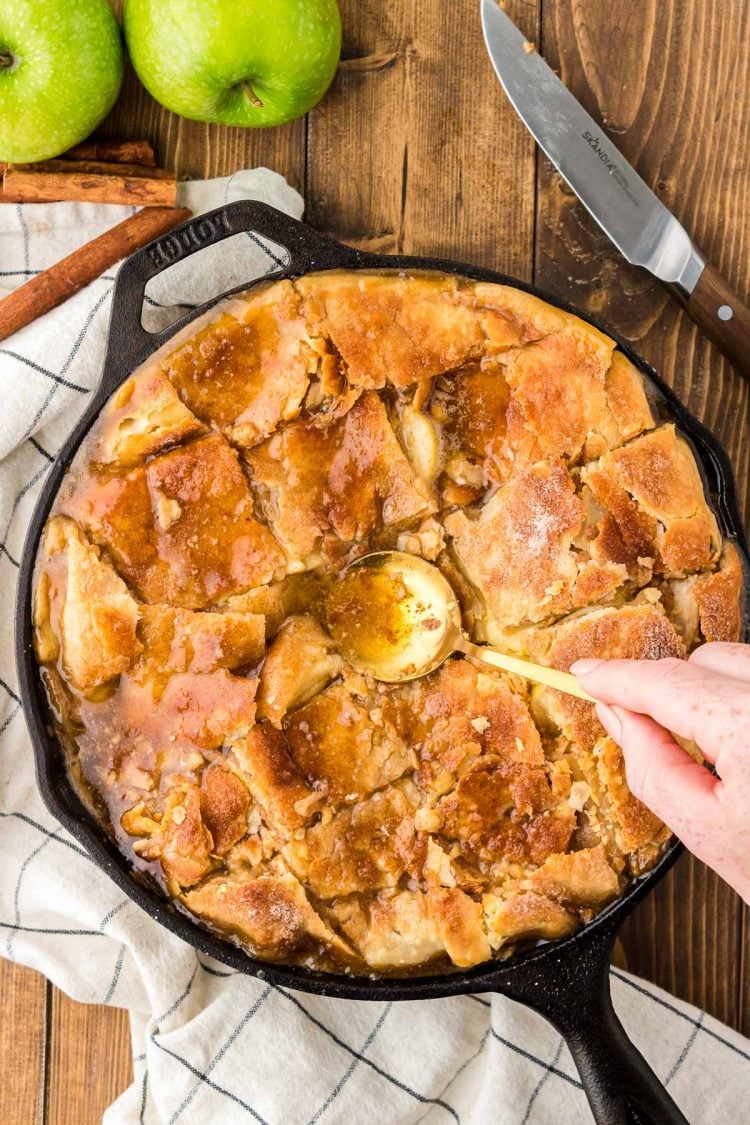 A spoon pressing pieces of cut pie crust into apple mixture.