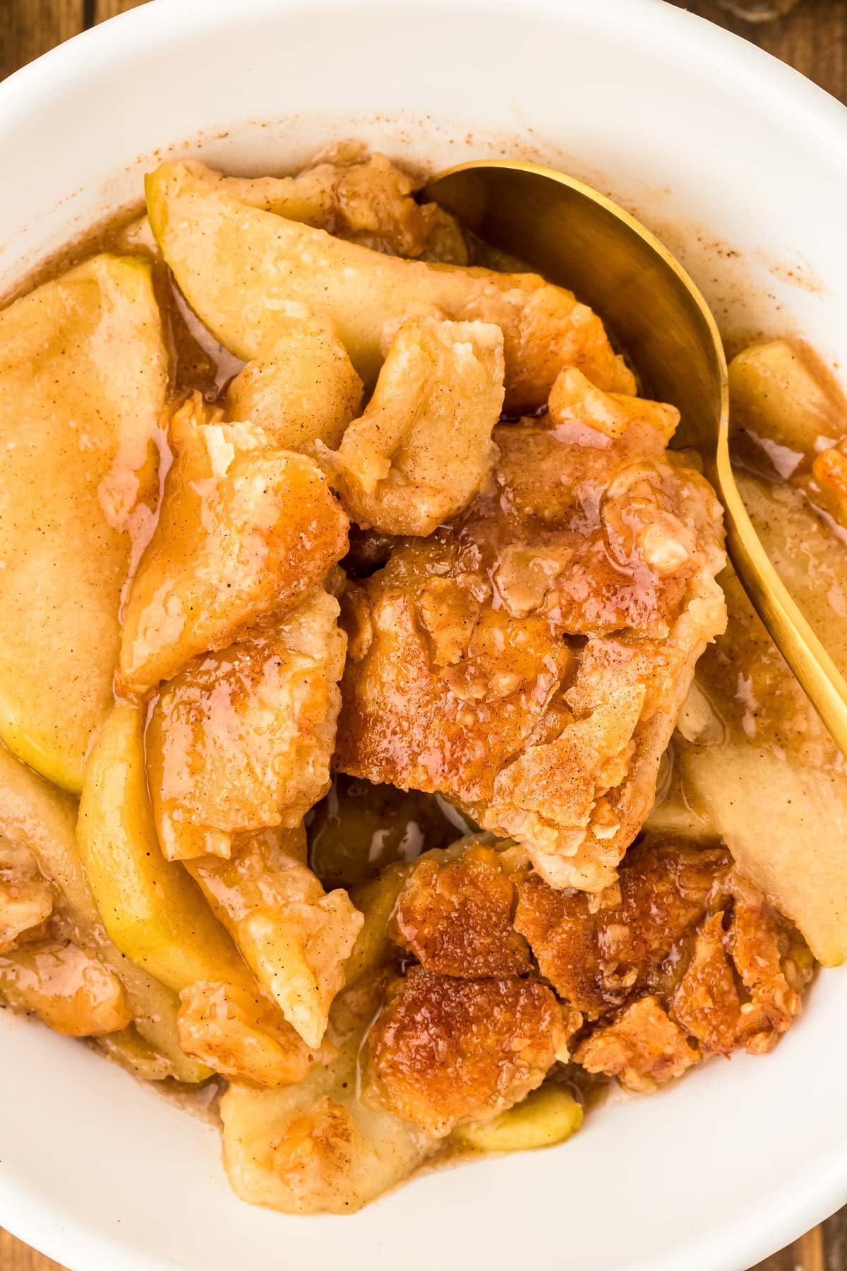 A white bowl filled with apple pan dowdy and a gold spoon.