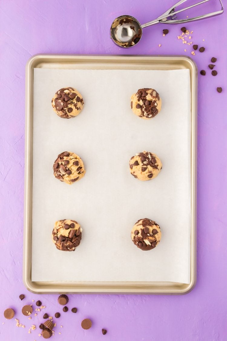 Balls of vanilla and chocolate cookie dough on a parchment lined baking sheet.
