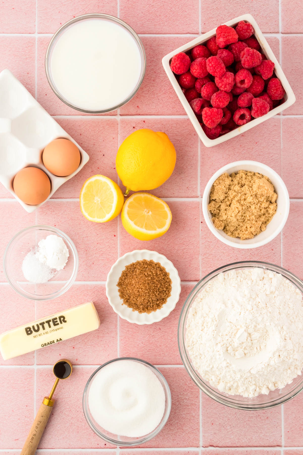 Overhead photo of ingredients prepped to make lemon raspberry cake on a pink surface.