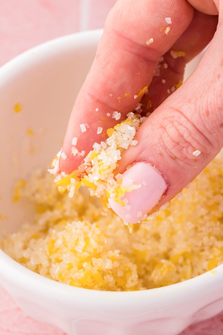 Lemon sugar being mixed by hand in a bowl.