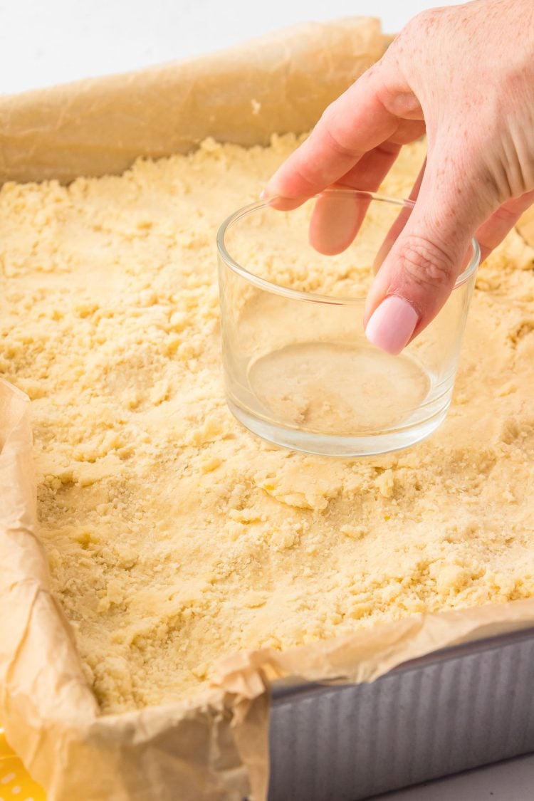A glass pressing shortbread cookies dough into a pan.
