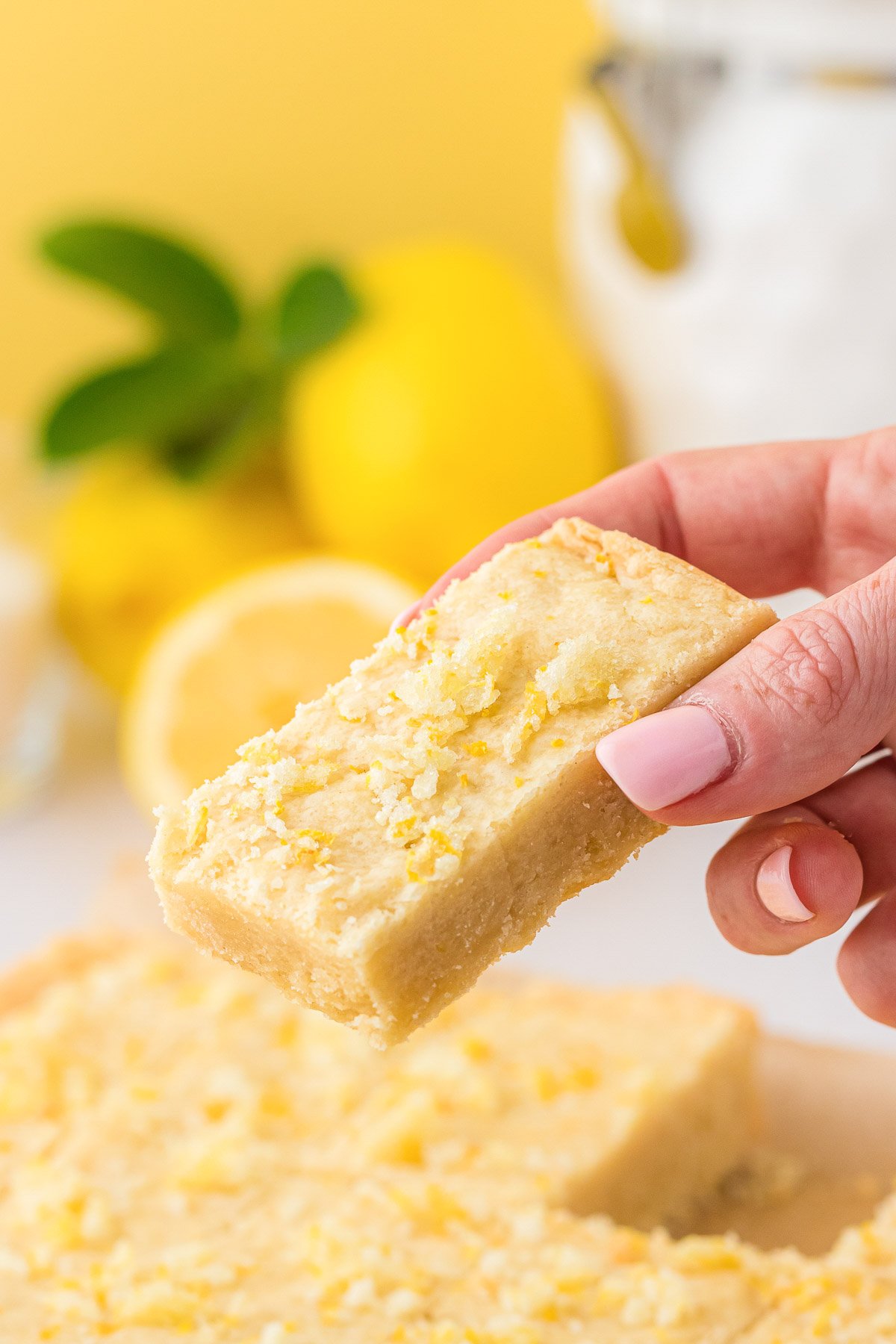 A woman's hand holding a lemon shortbread bar.