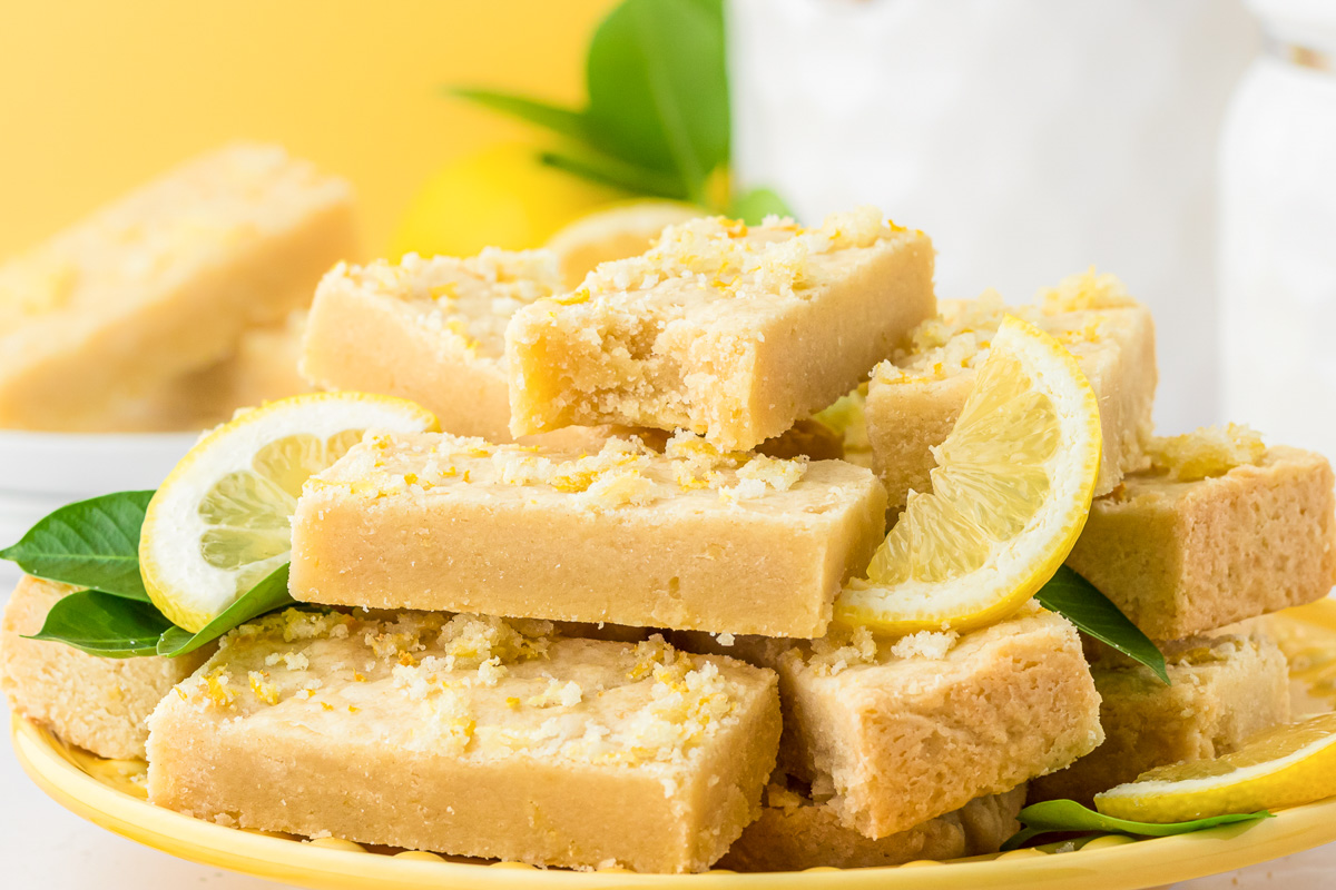 A plate of lemon shortbread bars with the top one missing a bite.