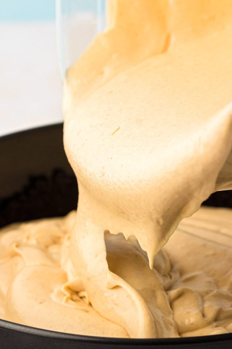 Peanut Butter cheesecake filling being poured into Oreo cheesecake crust. 