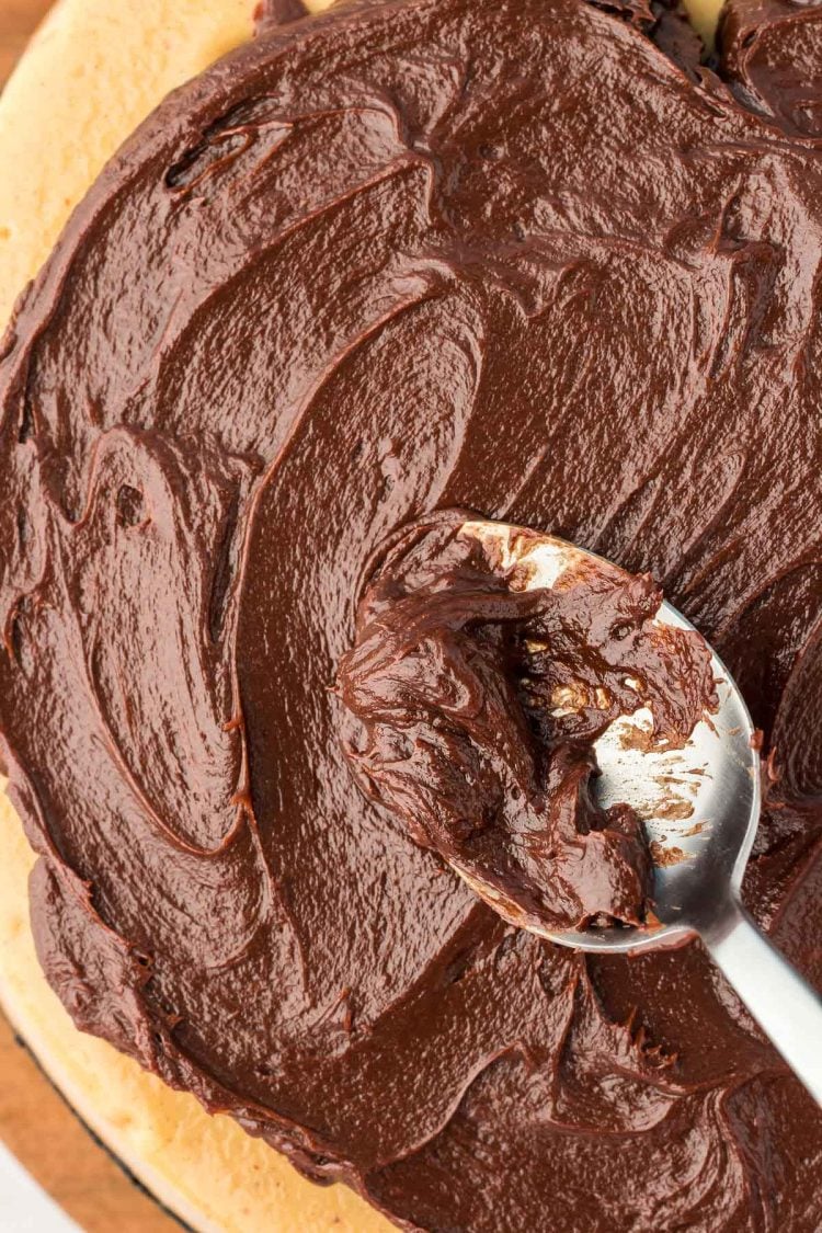 Ganache being spread over the top of a cheesecake with a spoon.