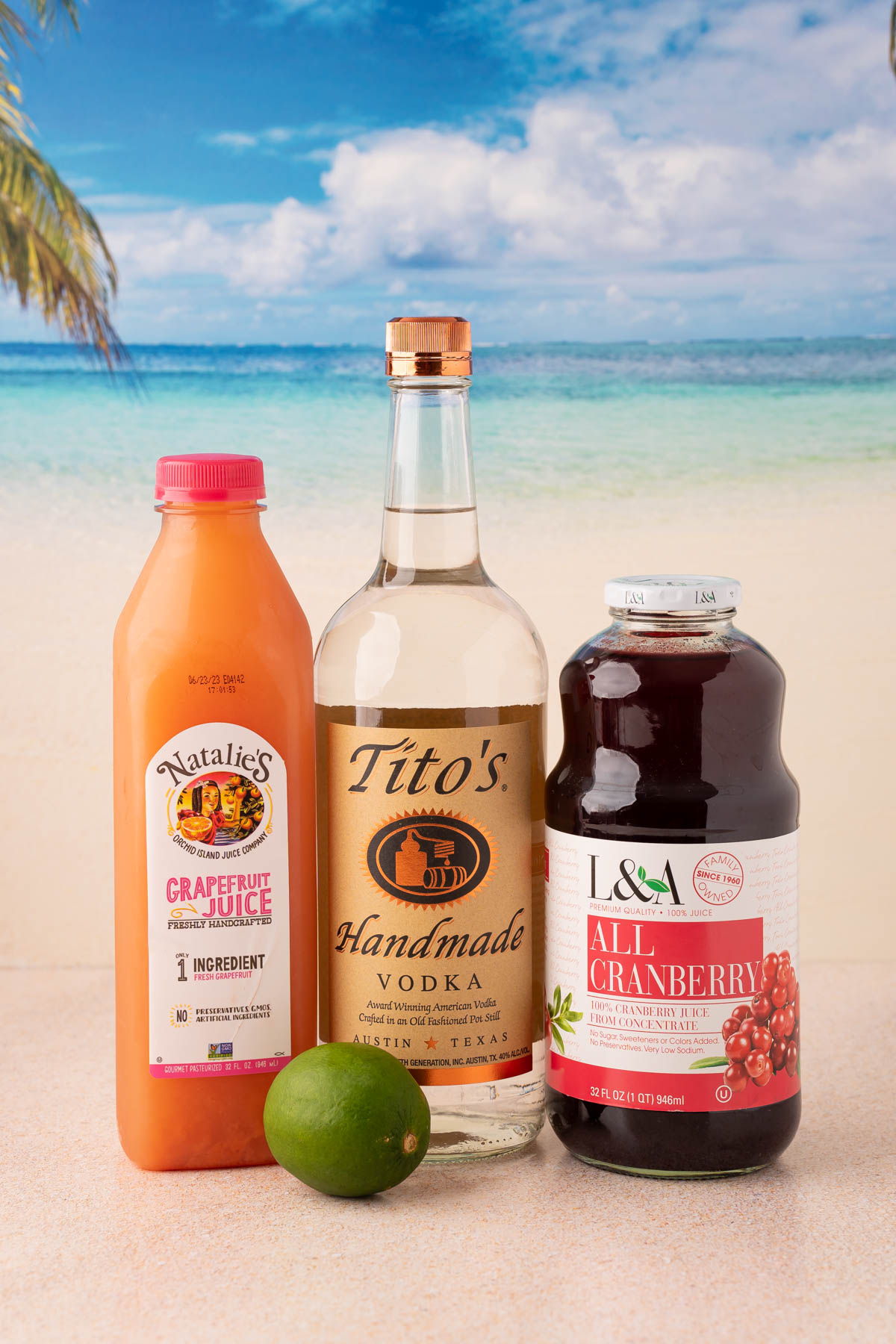 Bottles of grapefruit juice, vodka, and cranberry juice on a table with lime.