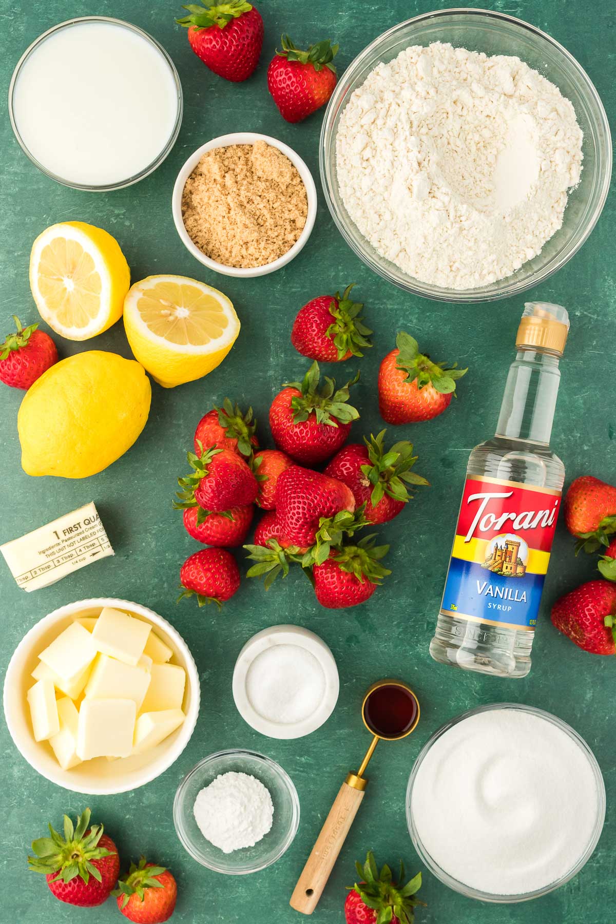 Ingredients to make strawberry cobbler on a green surface.