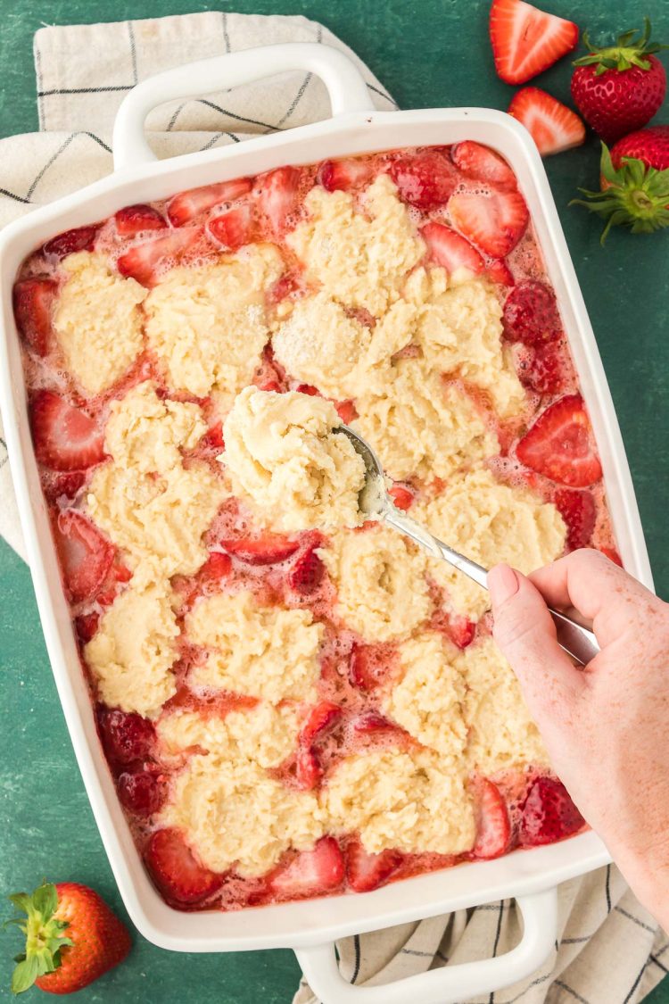 A woman's hand dolloping spoonfuls of biscuit topping on strawberry cobbler.