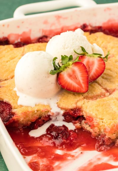 Two scoops of vanilla ice cream on a pan of strawberry cobbler.