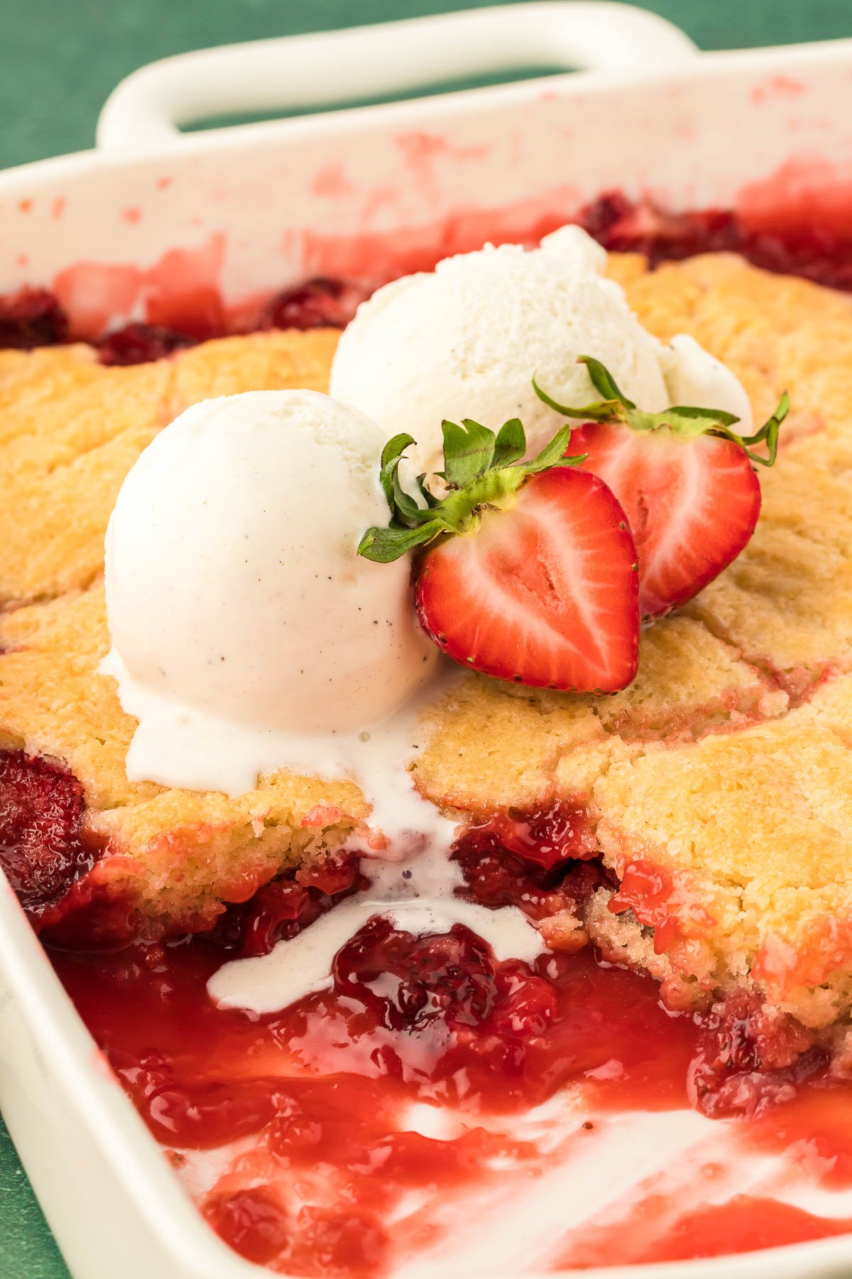 Two scoops of vanilla ice cream on a pan of strawberry cobbler.