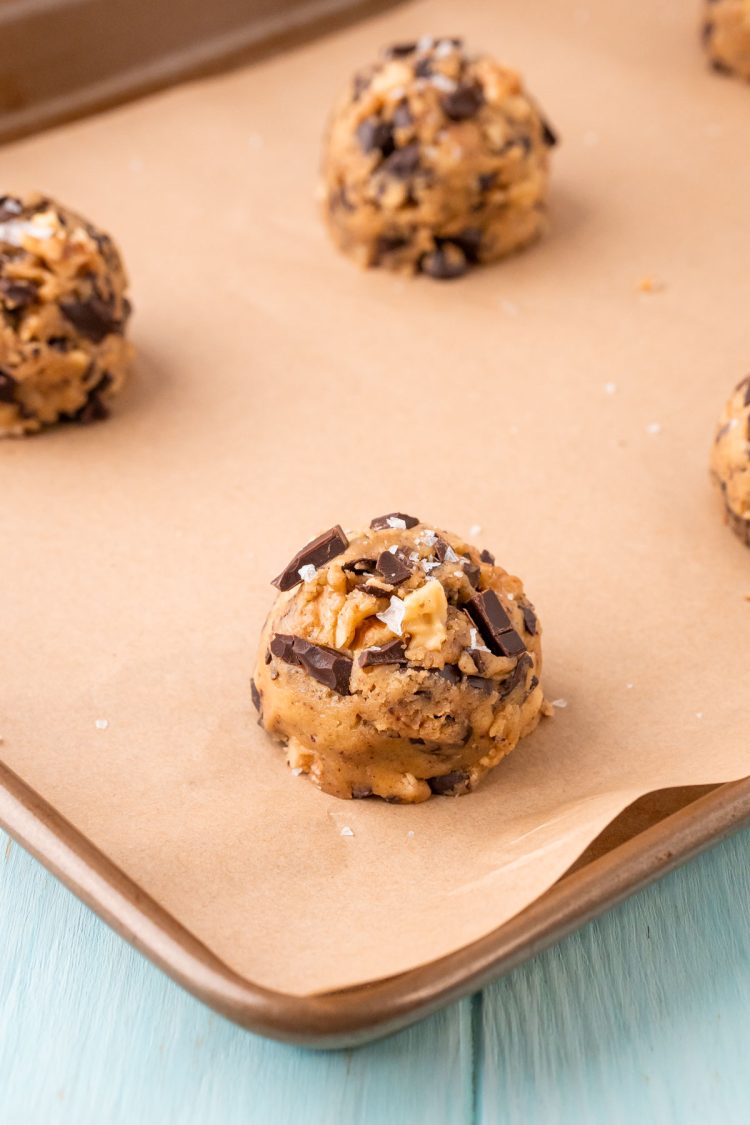 Balls of cookie dough on parchment paper on a baking sheet, ready to bake.