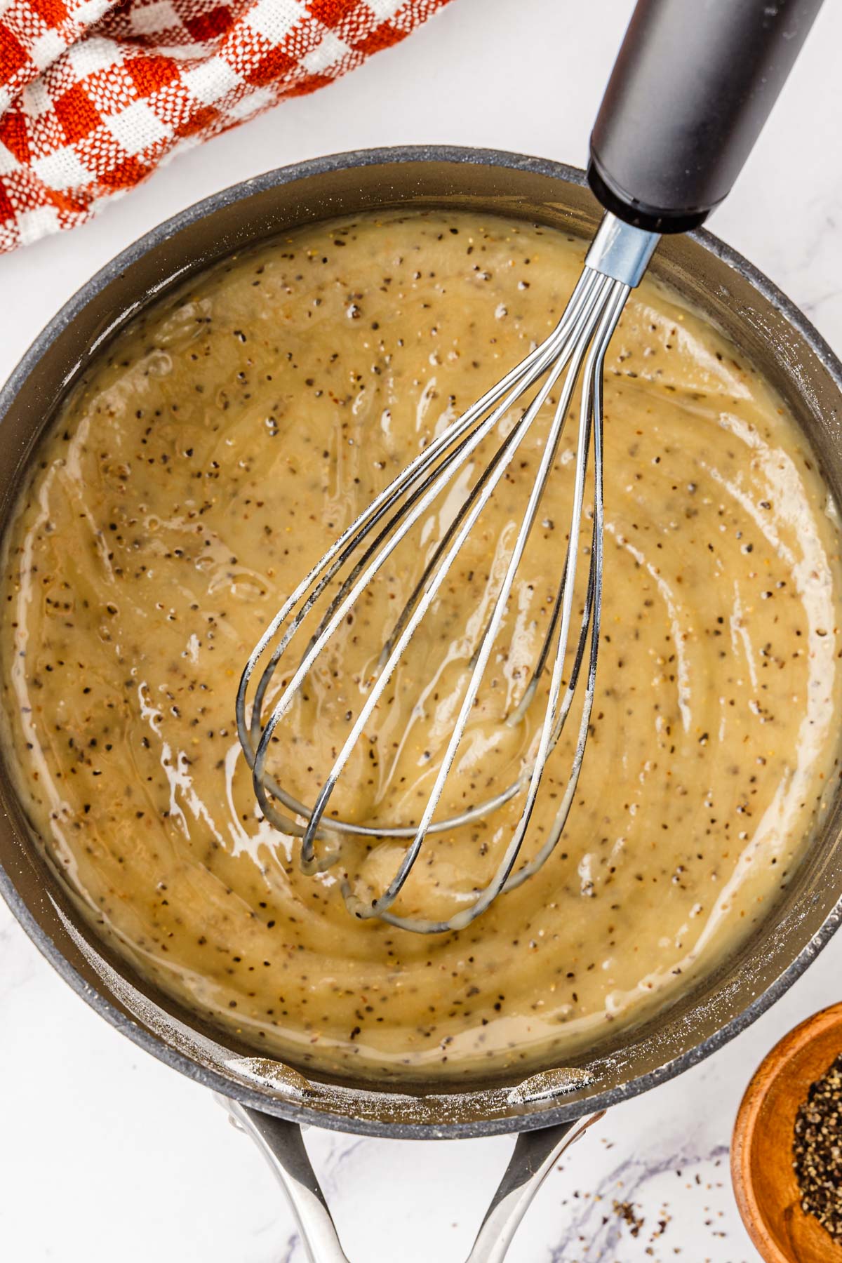 Flour, butter, and black pepper being whisked in a saucepan.