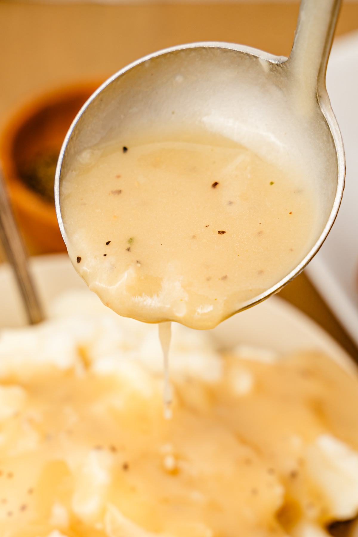 A ladle with turkey gravy pouring on mashed potatoes.