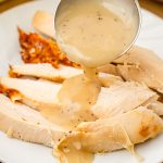 A ladle pouring gravy over turkey breast on a plate.