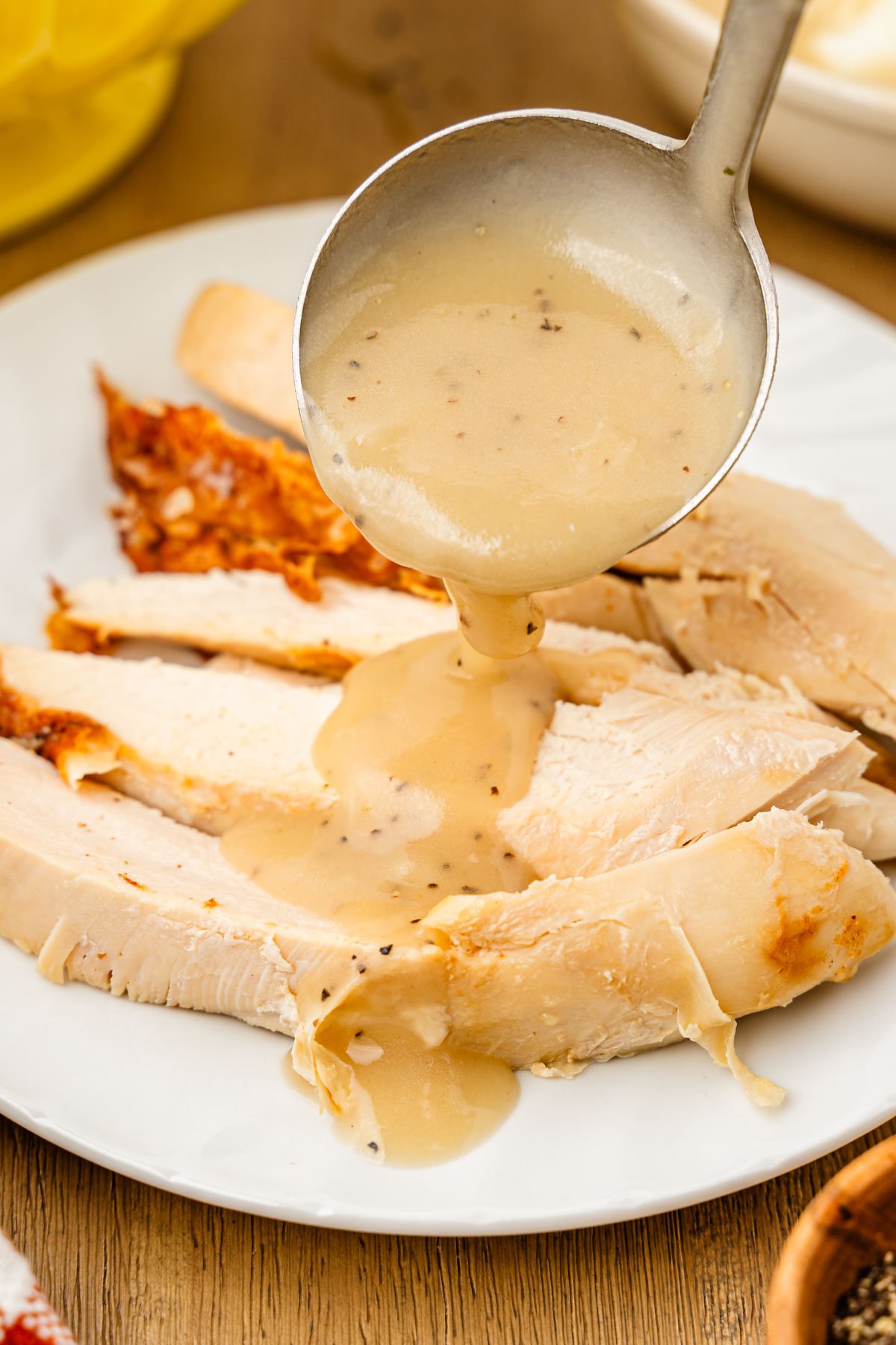 A ladle pouring gravy over turkey breast on a plate.