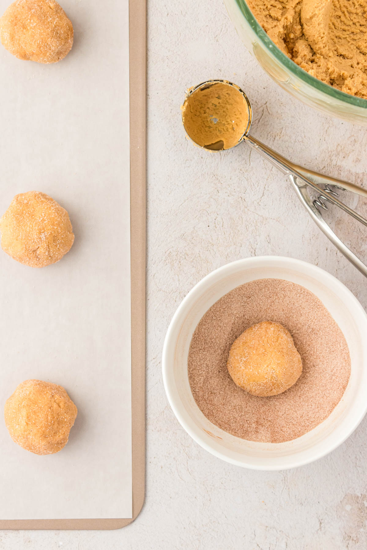 Cookie dough balls being rolled in cinnamon sugar and placed on a baking sheet.