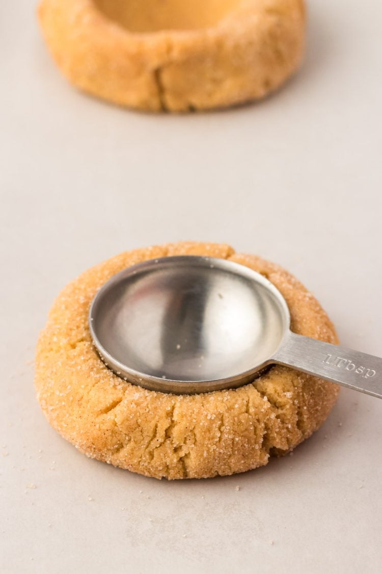 A tablespoon pressing into a ball of cookie dough.