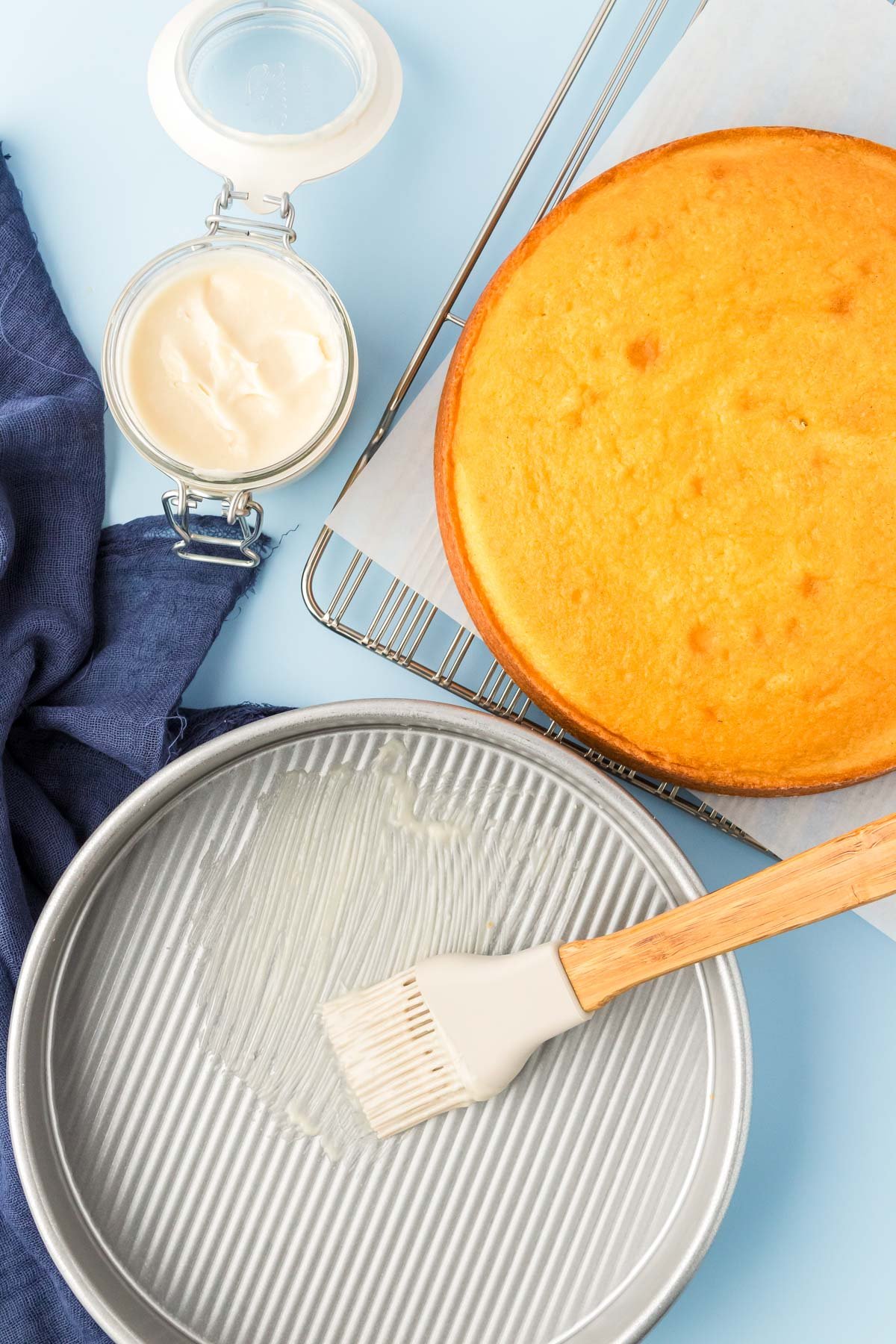 Cake goop being spread in a cake pan with a cake next to it.