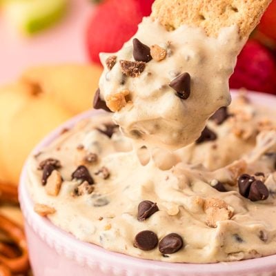 Close up of a graham cracker scooping into a bowl of chocolate chip cookie dough dip.