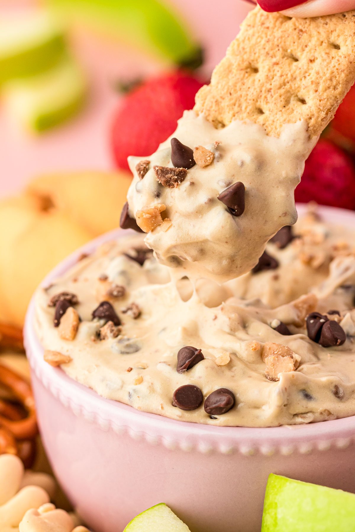 Close up of a graham cracker scooping into a bowl of chocolate chip cookie dough dip.