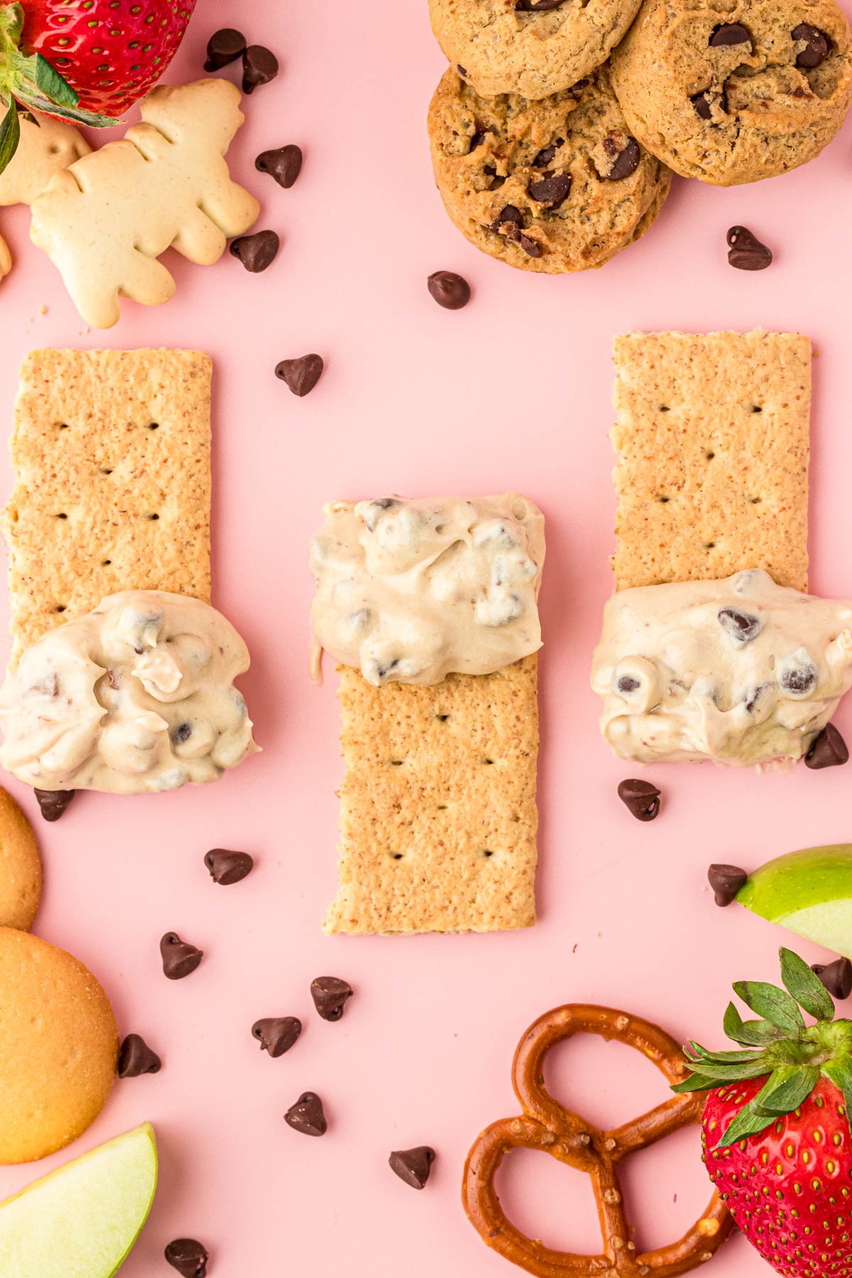 Graham crackers with cookie dough dip on them on a pink surface.