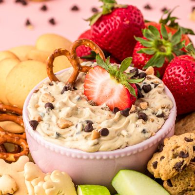 A bowl of chocolate chip dip surrounded bu fruit and cookies for dipping.