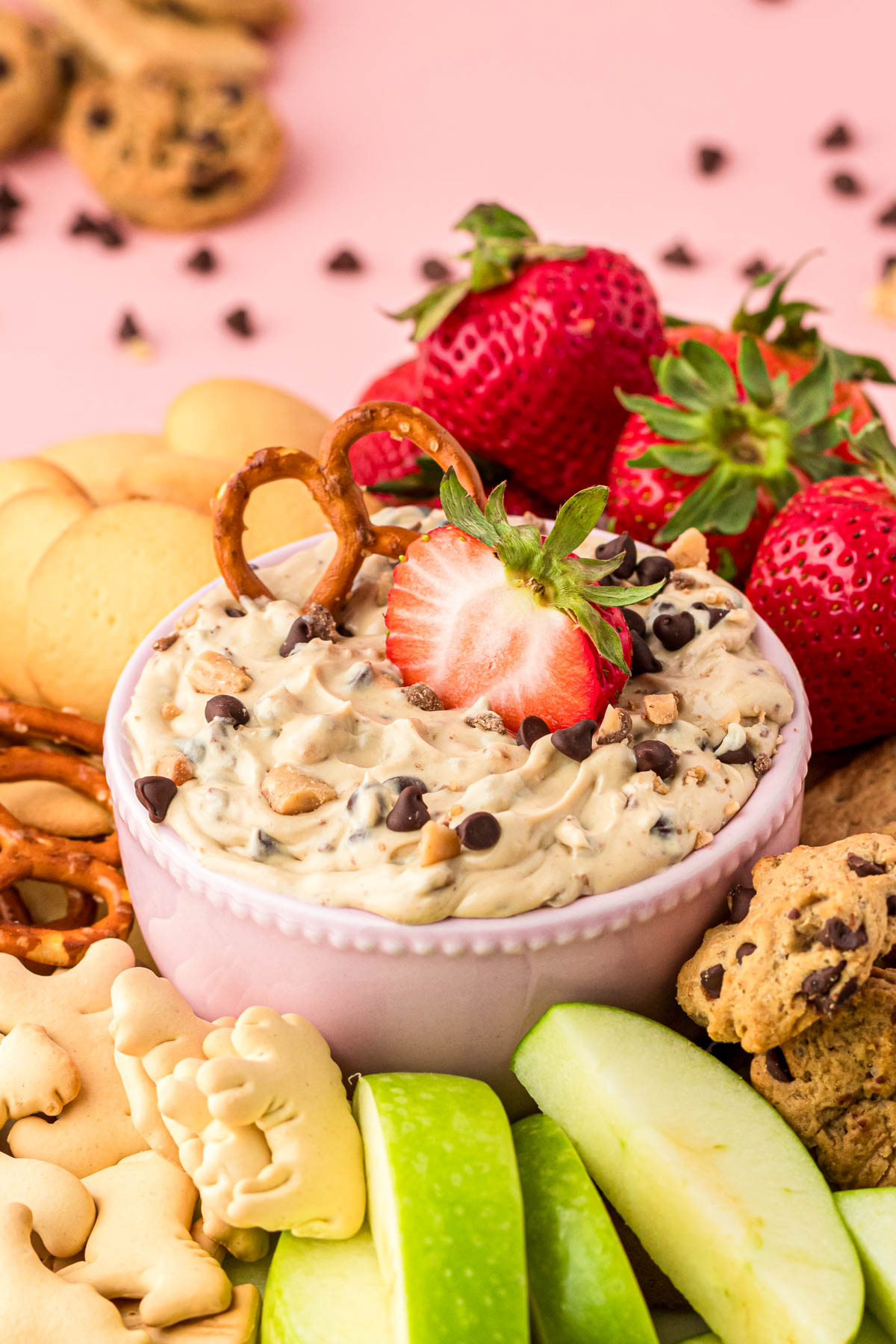 A bowl of chocolate chip dip surrounded bu fruit and cookies for dipping.