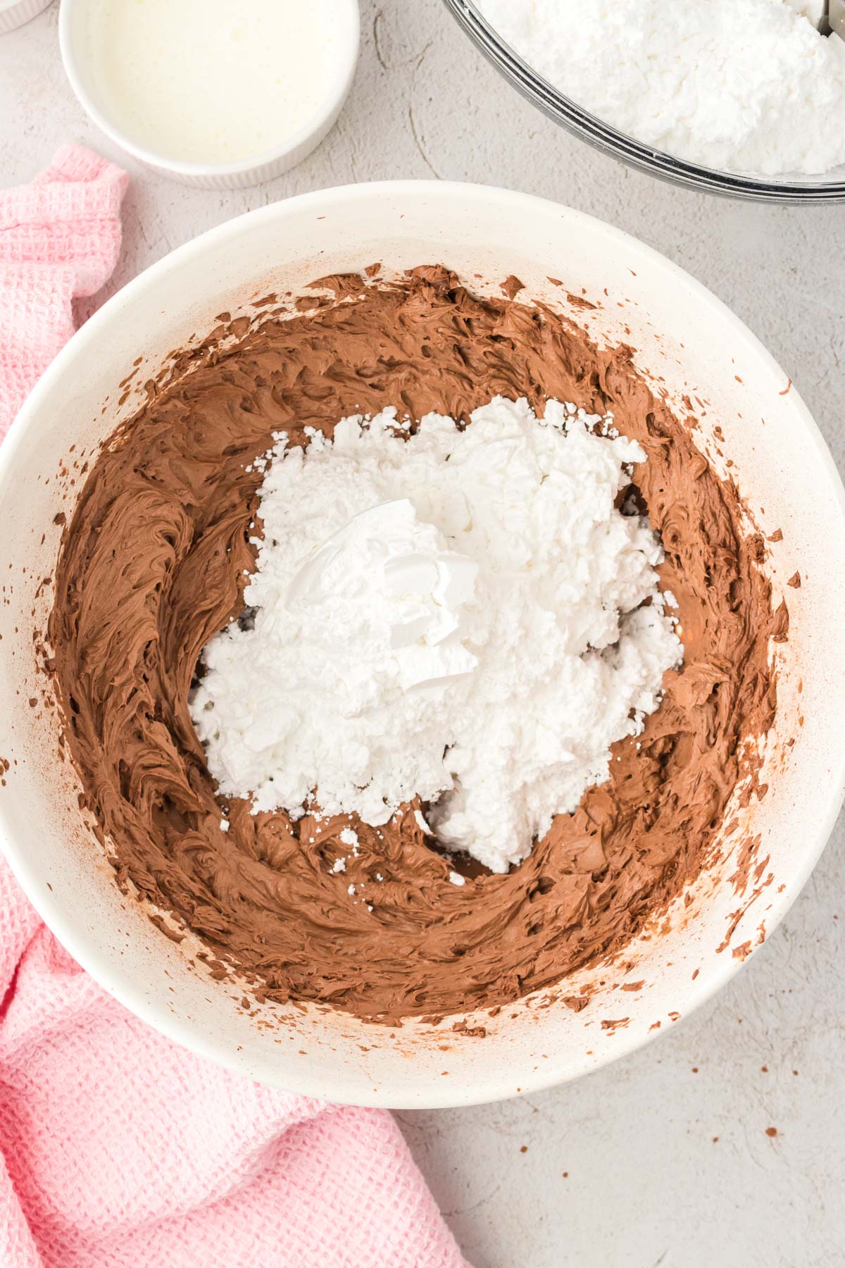 Powdered sugar being added to a bowl with chocolate frosting base.