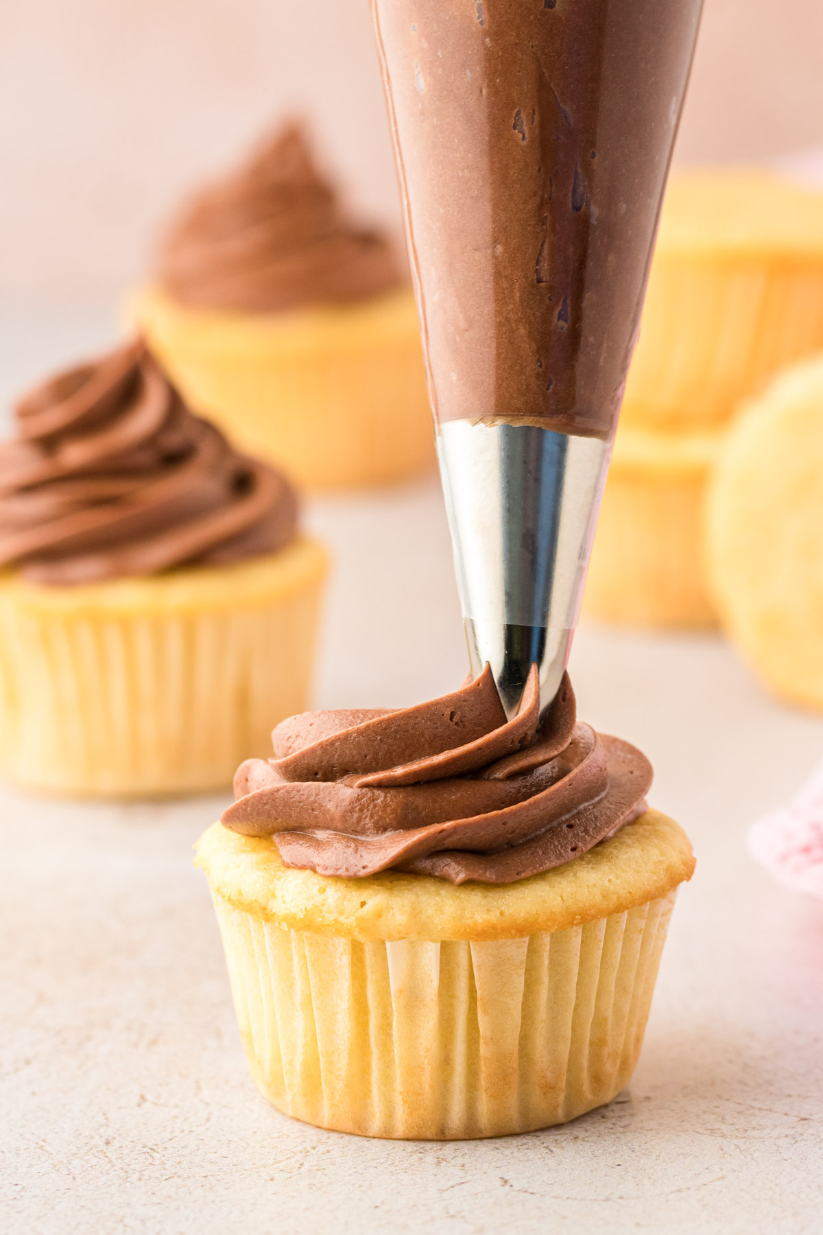 Chocolate cream cheese frosting being piped onto a yellow cupcake.