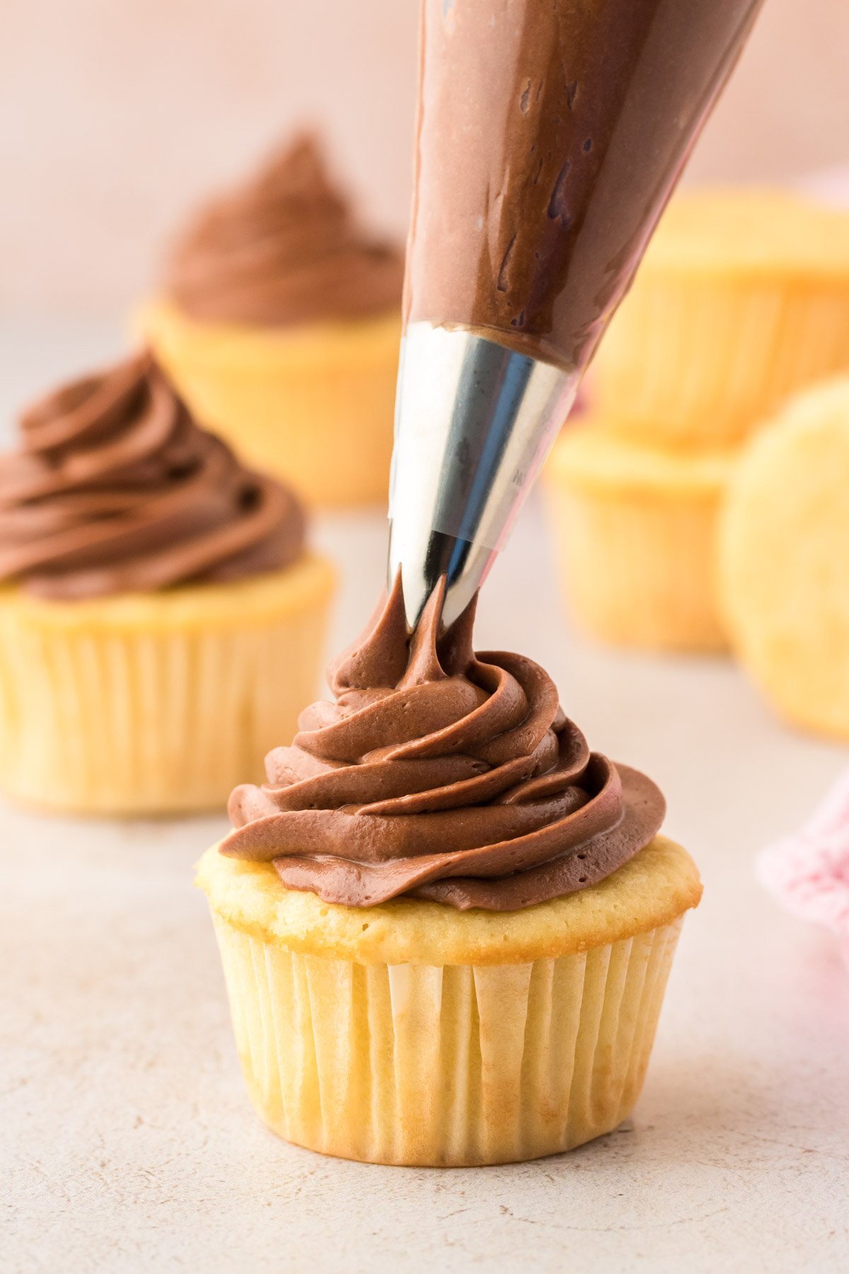 Chocolate cream cheese frosting being piped onto a yellow cupcake.