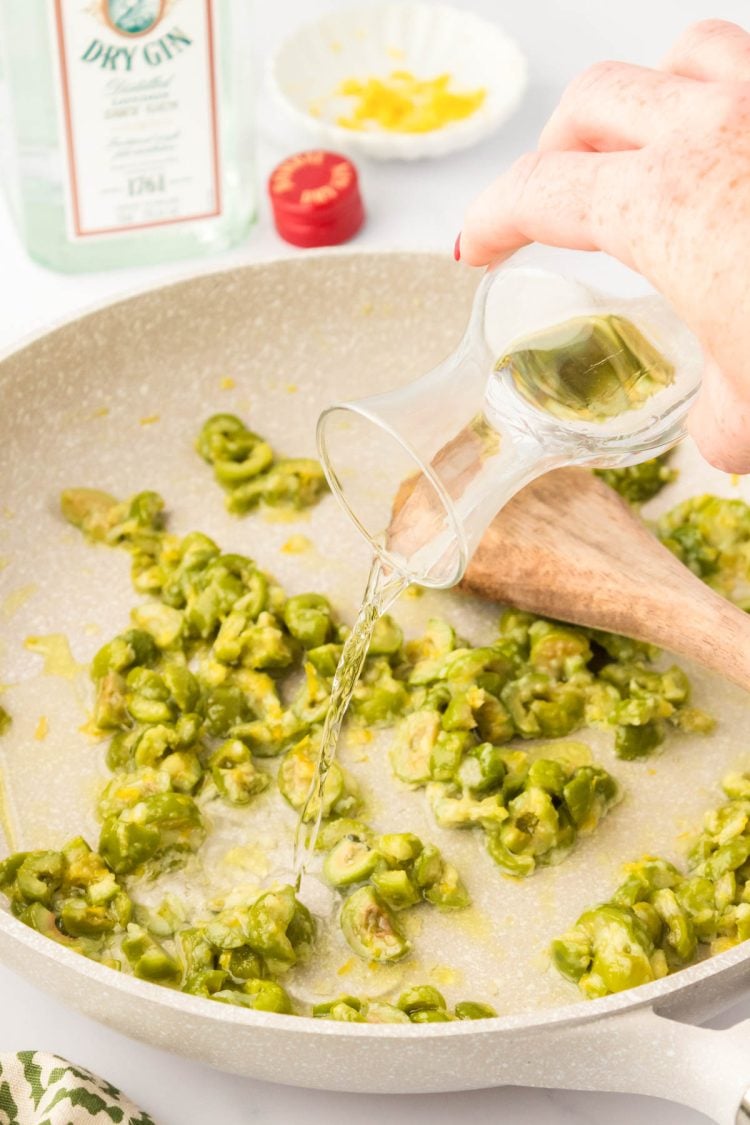 Gin being poured into a skillet with olives and lemon zest.