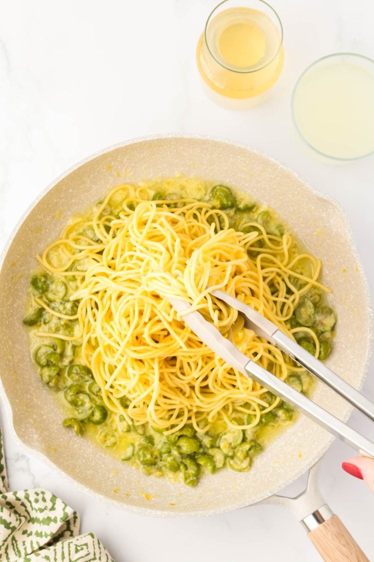 Pasta being added to a skillet with olives.