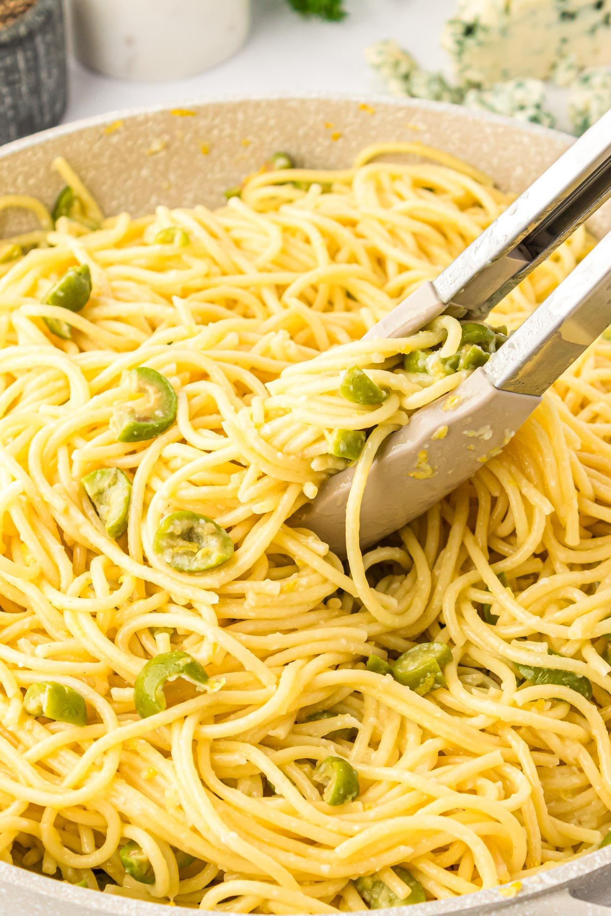 Dirty Martini pasta in a skillet with tongs getting ready to serve it.