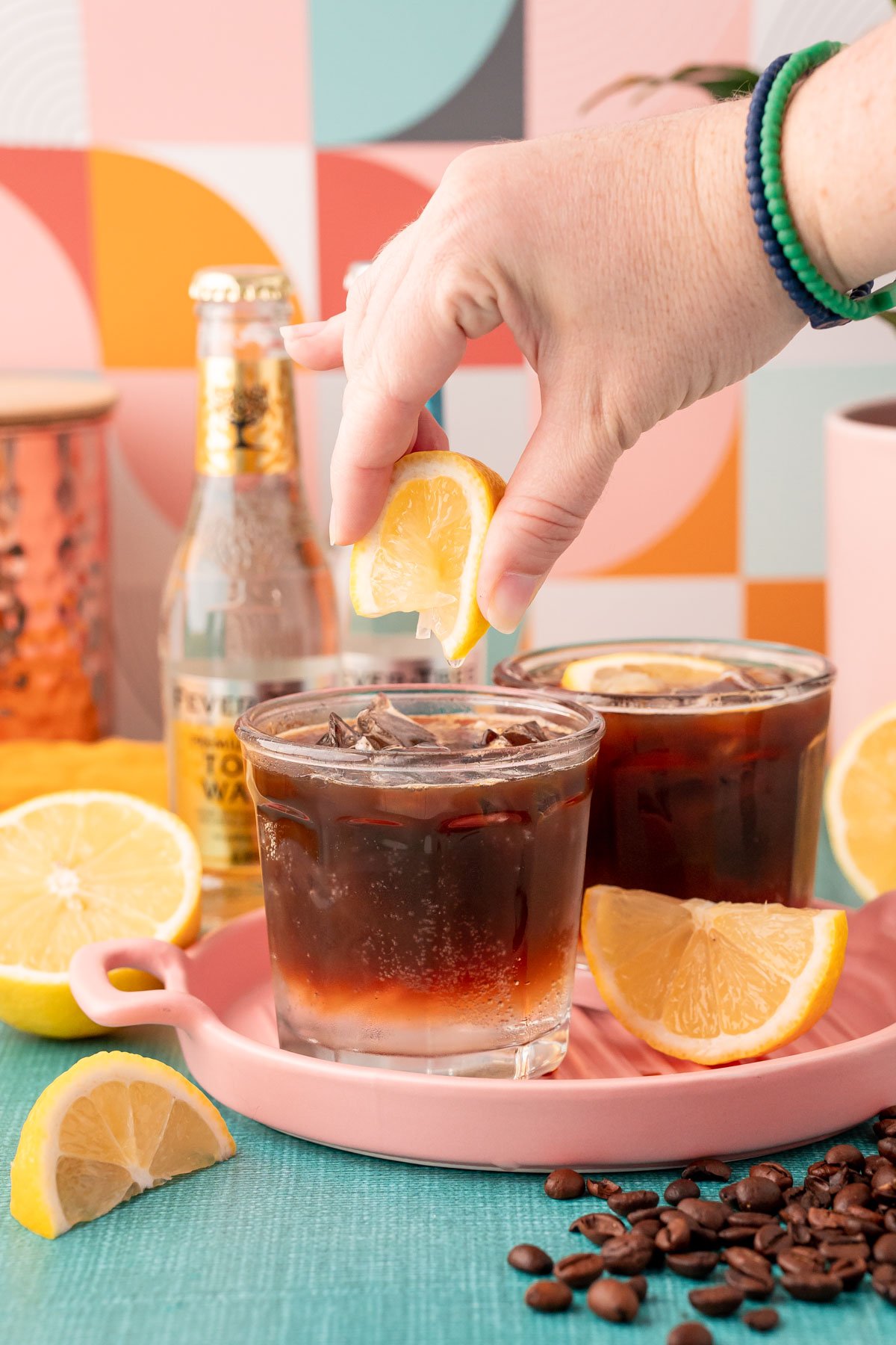 A lemon wedge being squeezed into a glass with espresso and tonic.