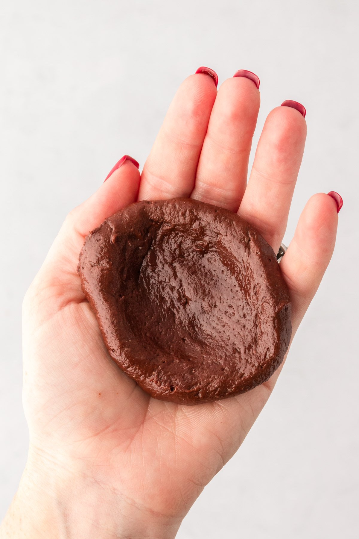 Chocolate cookie dough in a woman's hand in a bowl shape.