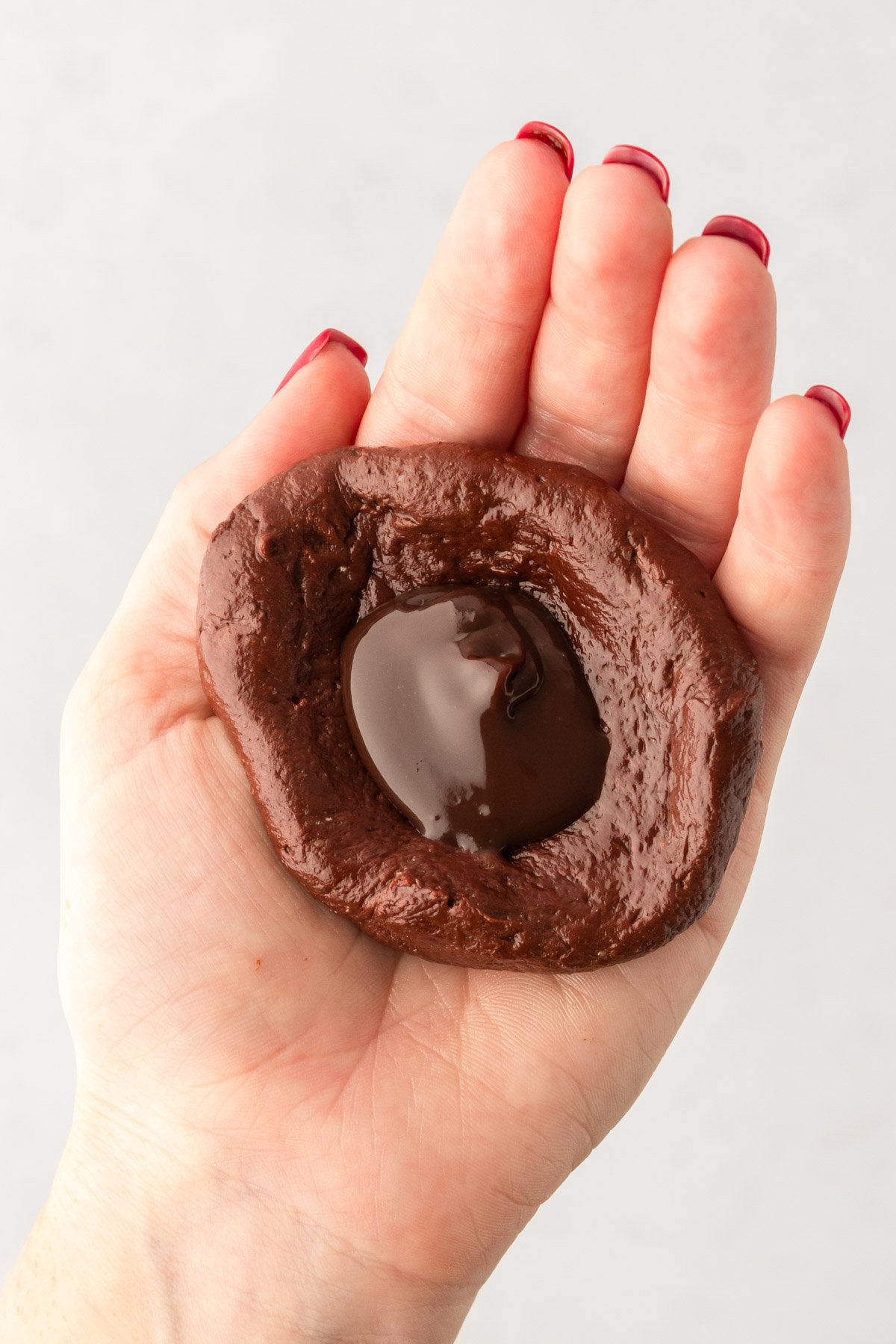 A scoop of hot fudge in the center of chocolate cookie dough in a woman's hand.