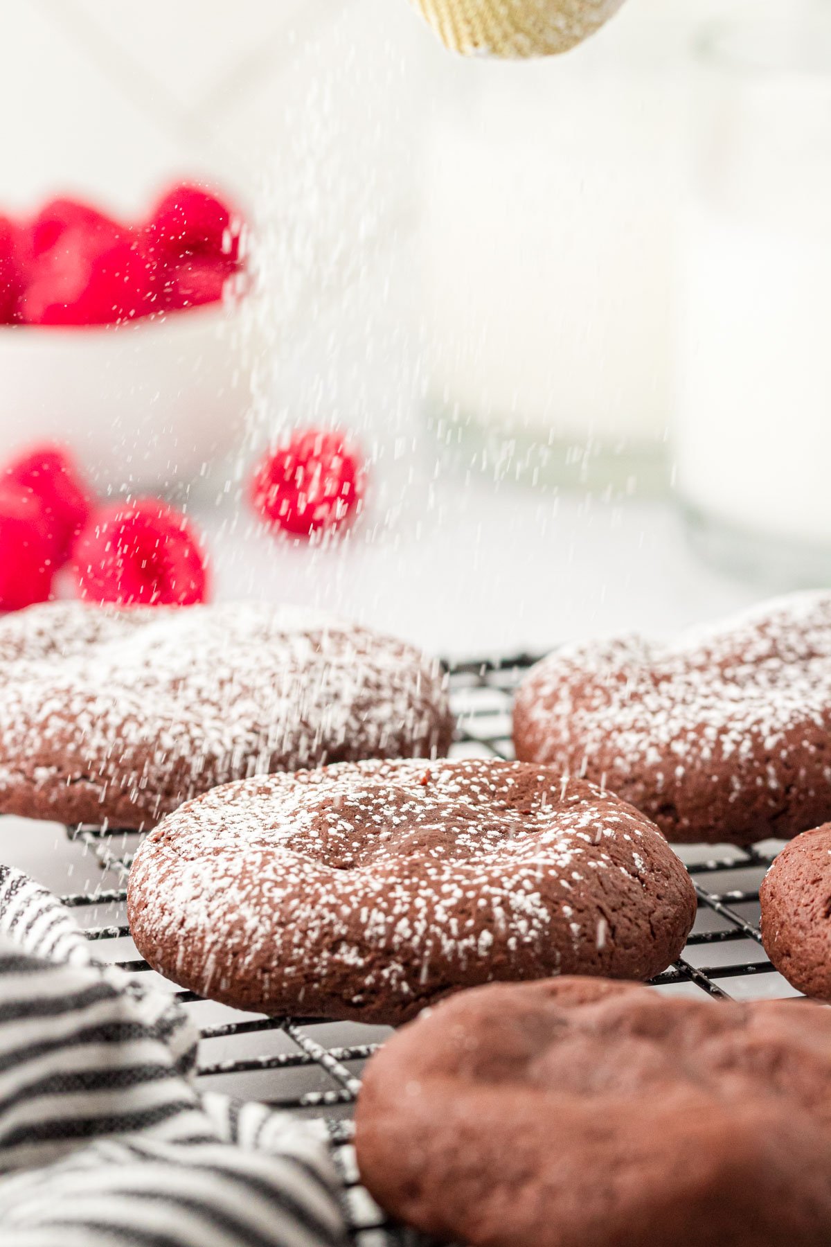 Chocolate cookies on a wire rack being dusted with powdered sugar.