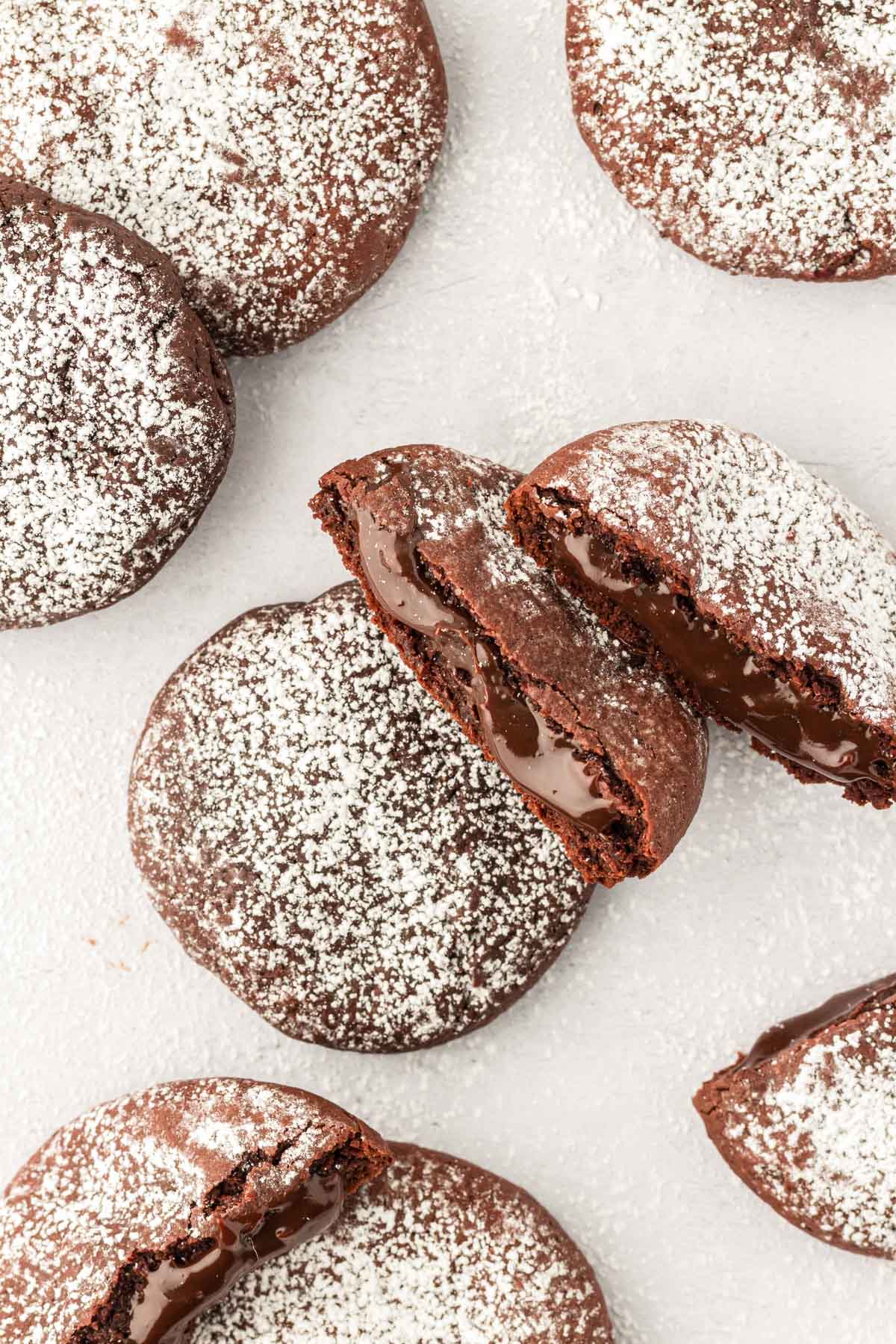 Overhead photo of molten lava cake cookies on a white table, some broken in half to reveal the gooey center.
