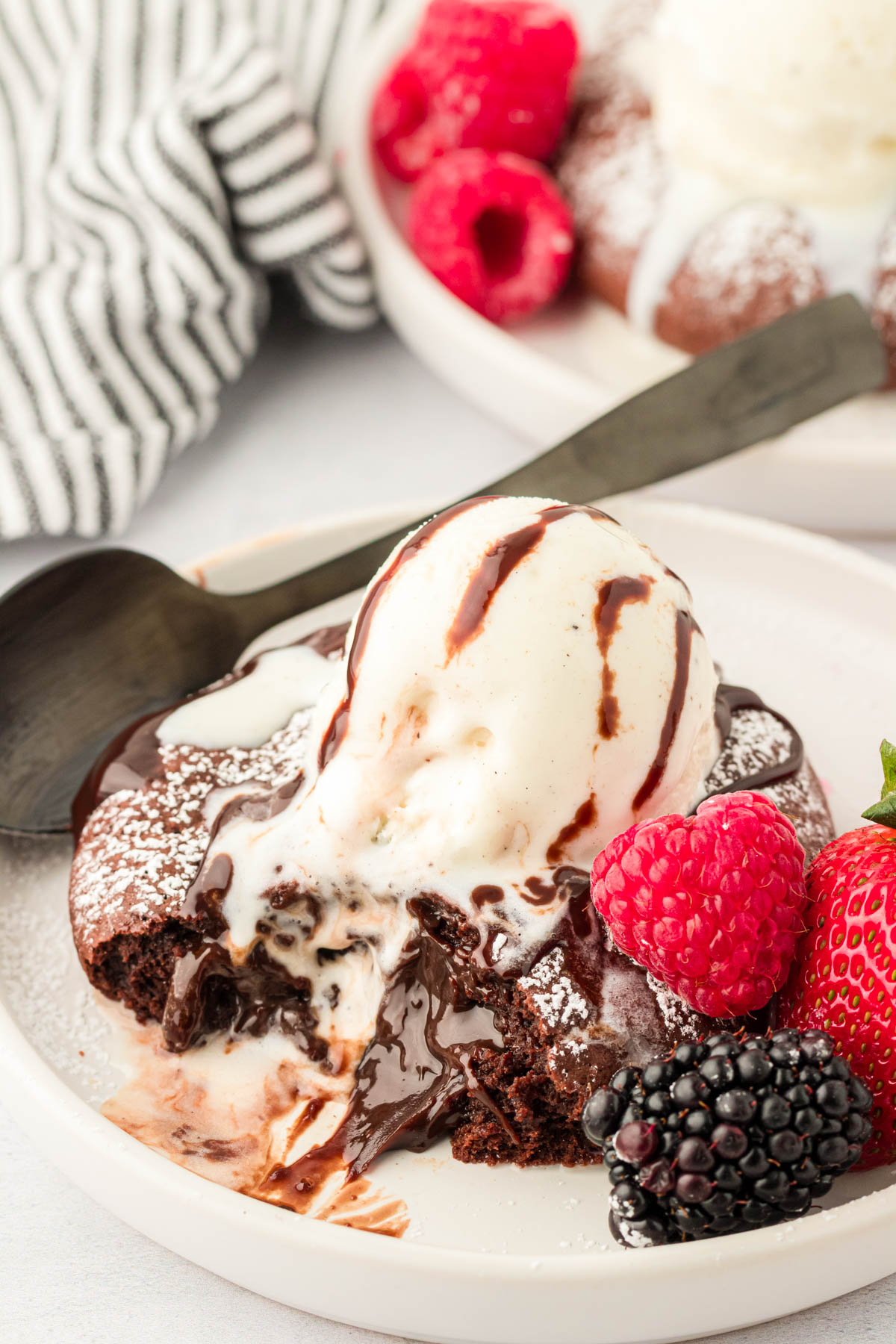 A large lava cake cookie on a white plate with berries around it and a scoop of vanilla ice cream on top.