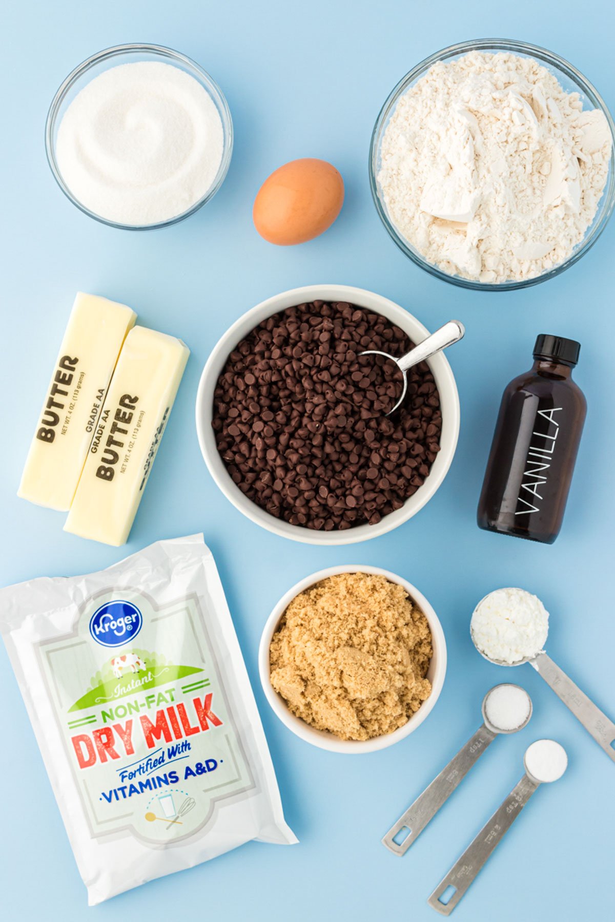 Overhead photo of ingredients to make mini chocolate chip cookies on a blue surface.